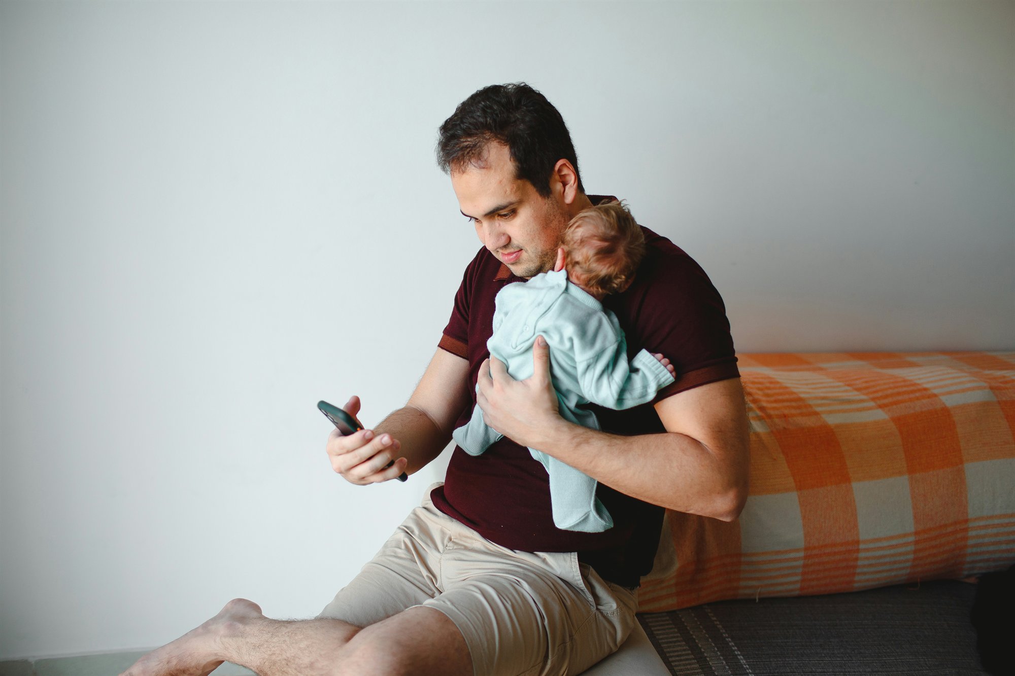 New parent holding a baby while checking their phone