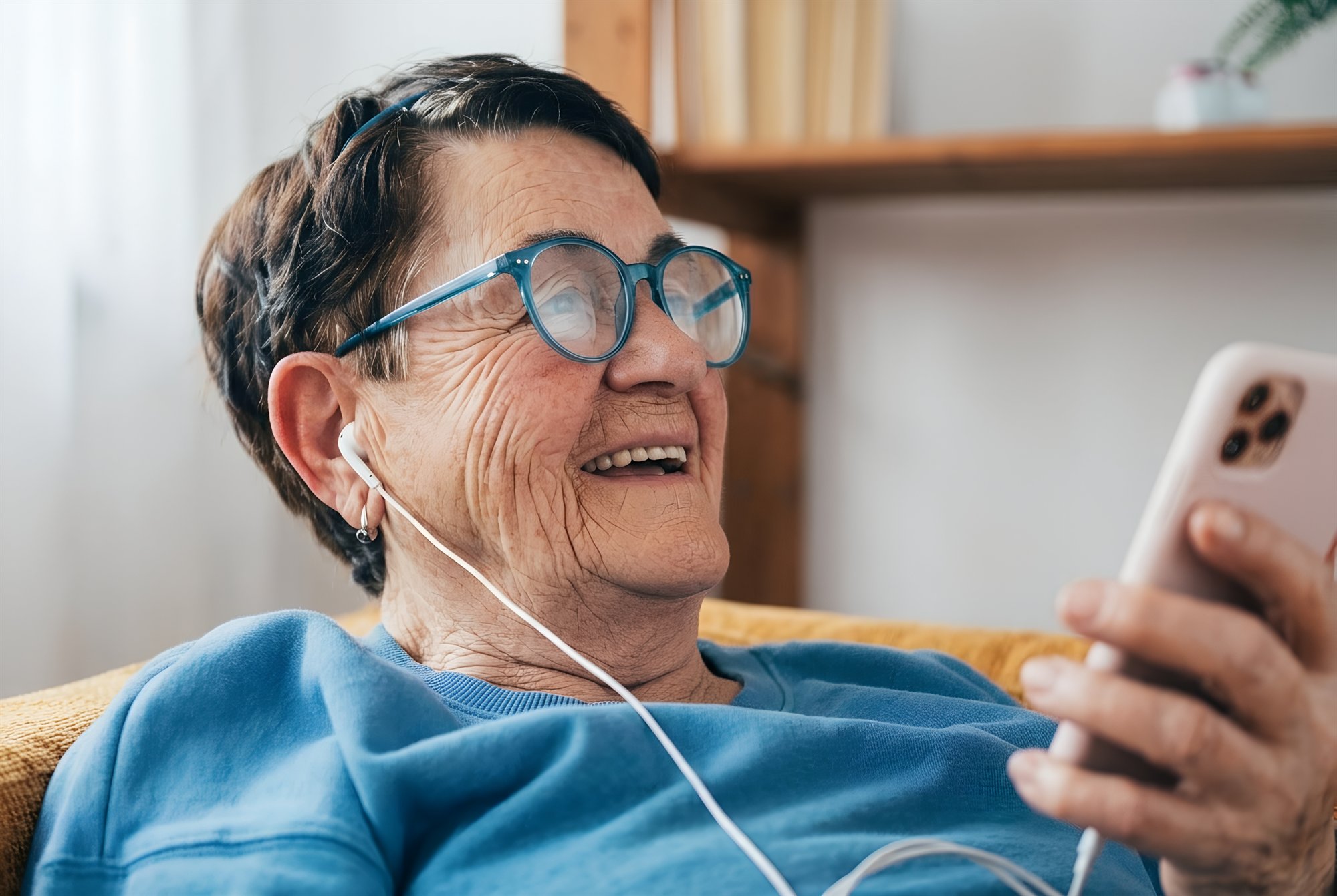 Senior woman smiling while using her phone, wearing glasses and earbuds