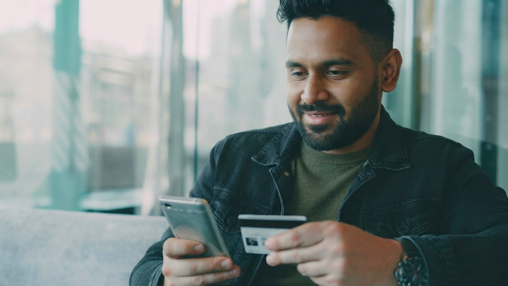 Man smiling while paying with his credit card on his phone