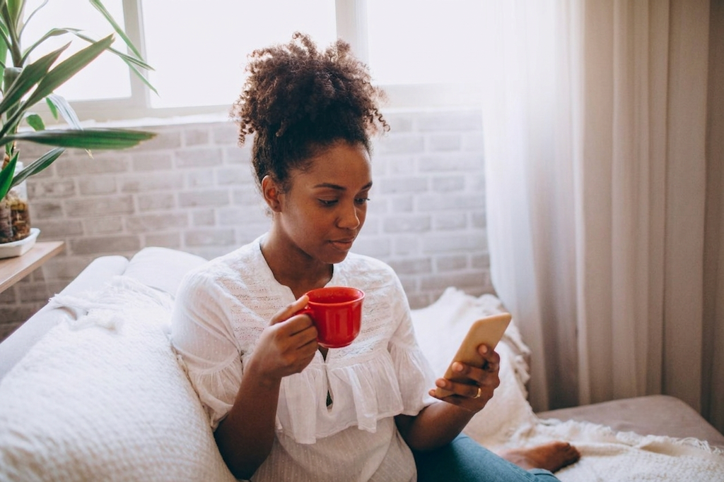 Woman relaxing on a sofa with coffee, looking at her phone